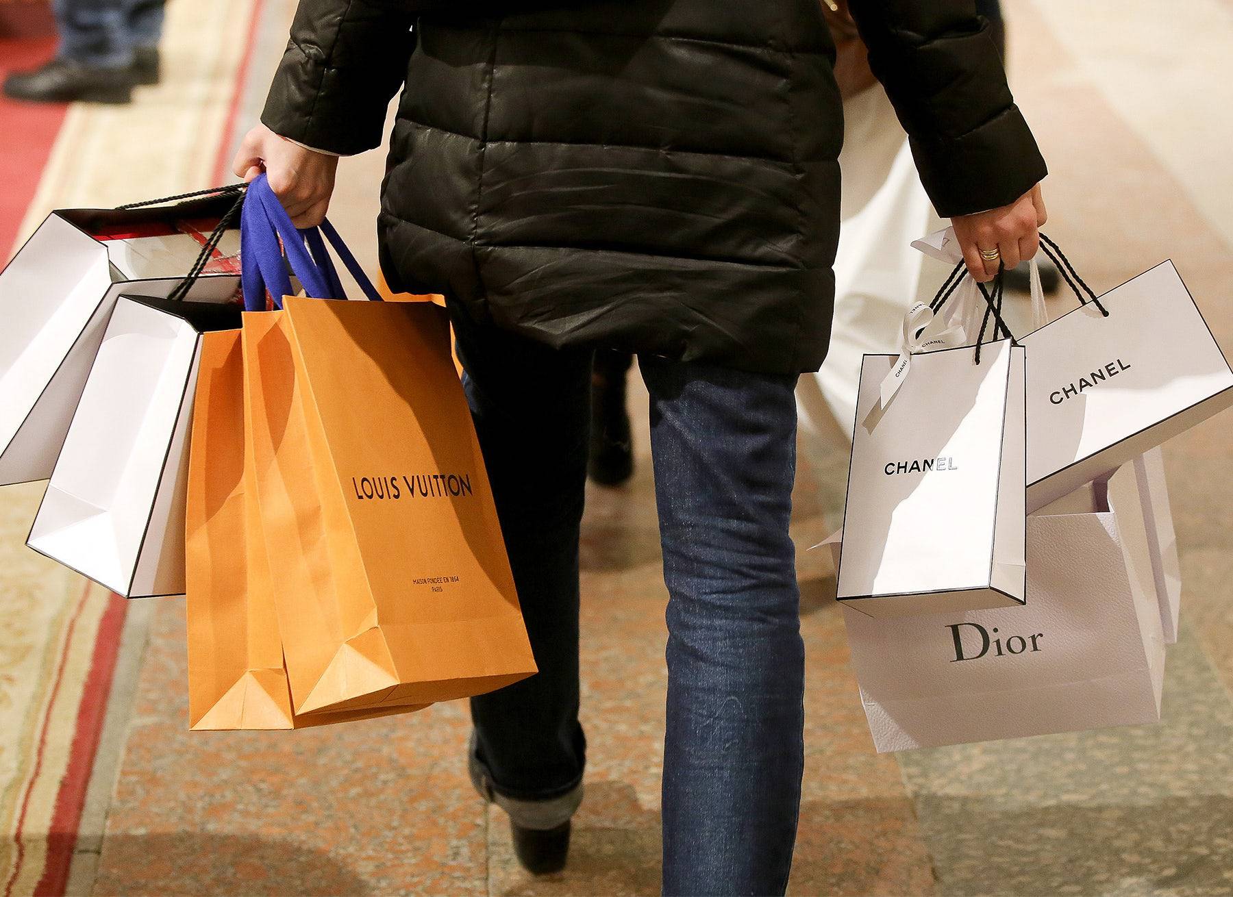 Person holding shopping bags in each hand, from luxury stores Dior, Chanel and Louis Vuitton.