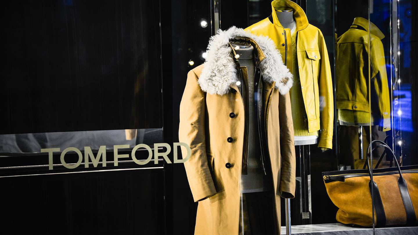 Tom Ford store front, featuring the brand name in gold and two cream and yellow jackets and a weekend bag.
