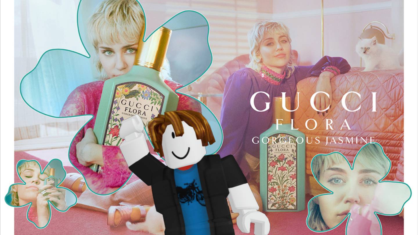 A Roblox avatar smiles and waves at the camera in front of a colourful ad for the Gucci Flora fragrance featuring Miley Cyrus.