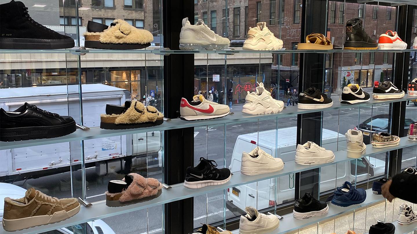 Sneakers are lined up in a window display with a New York City street in the background.