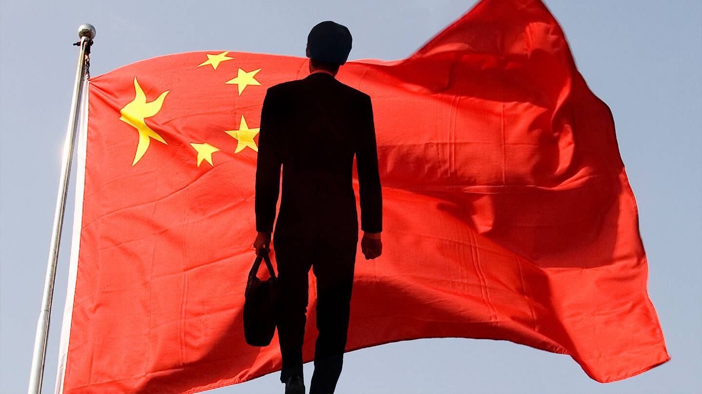 A man in a black suit with a briefcase standing in front of a Chinese flag.
