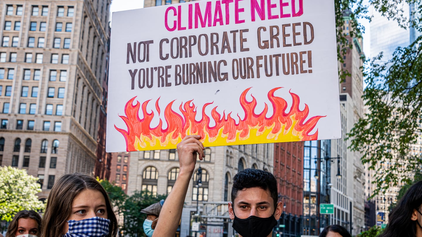 A protester holds up a sign saying "climate need, not corporate greed. You're burning our future!" during New York Climate Week last year.