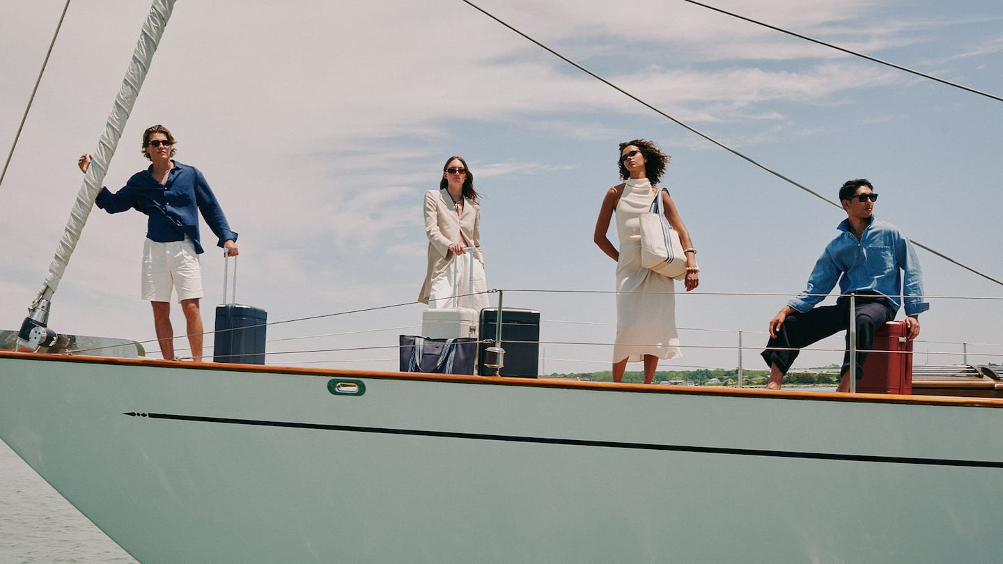 Travellers with luggage stand on a boat and gaze at the sky in a Paravel campaign inspired by Coastal New England.