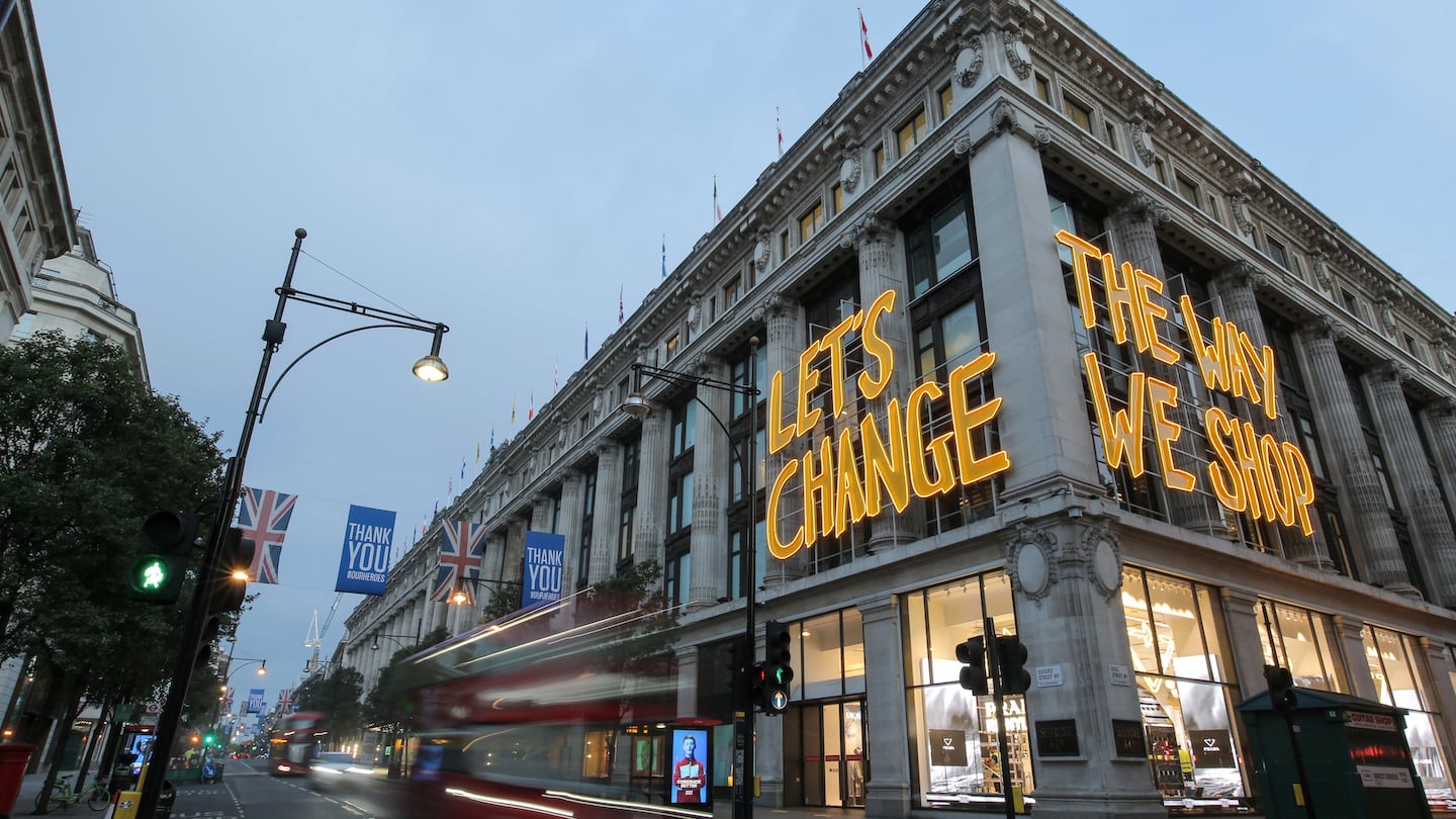 A sign lit up in yellow saying "let's change the way we shop" hangs on the facade of the Selfridges store on London's Oxford Street.