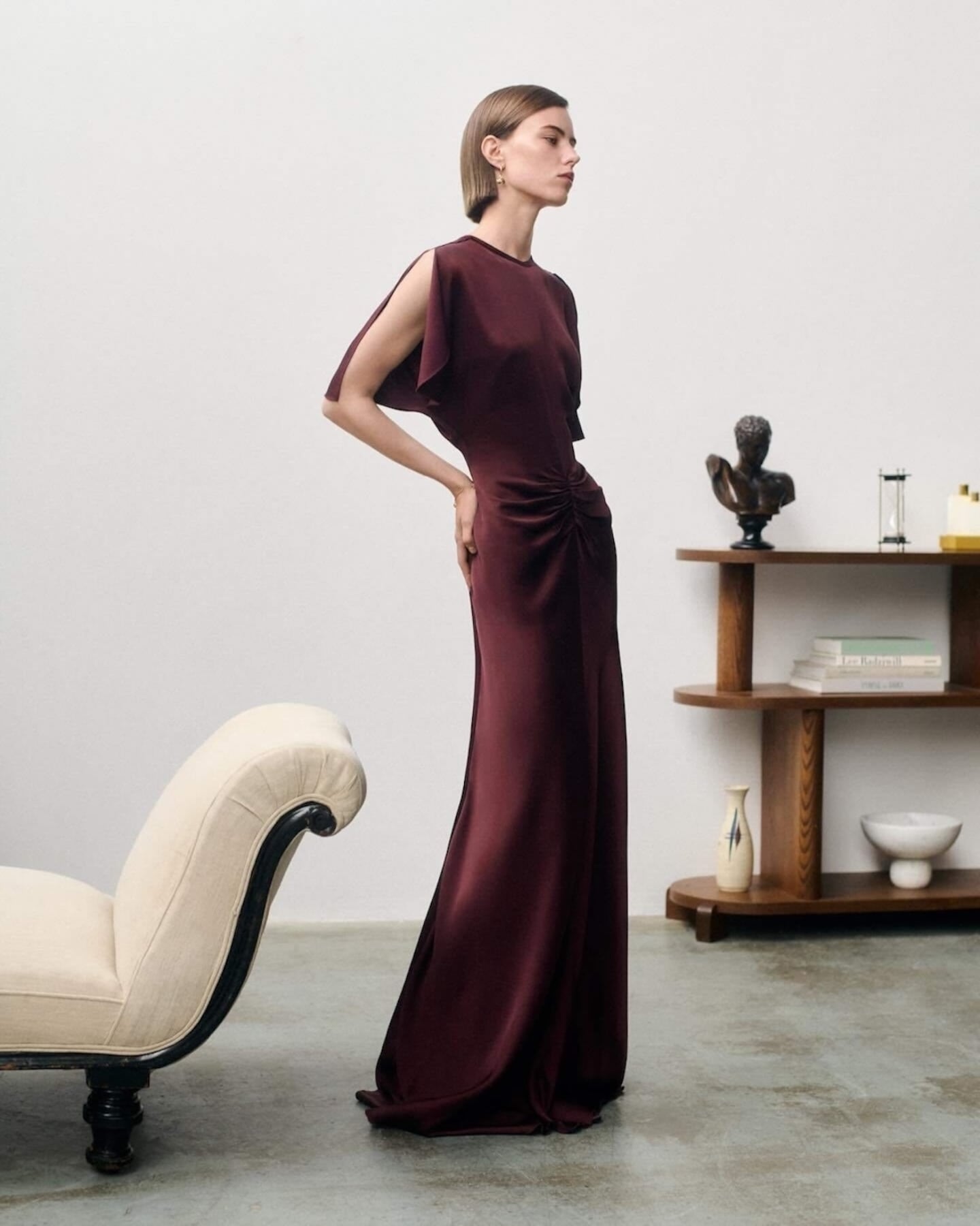 A model on a sparsely decorated set wears a burgundy evening column dress by Victoria Beckham