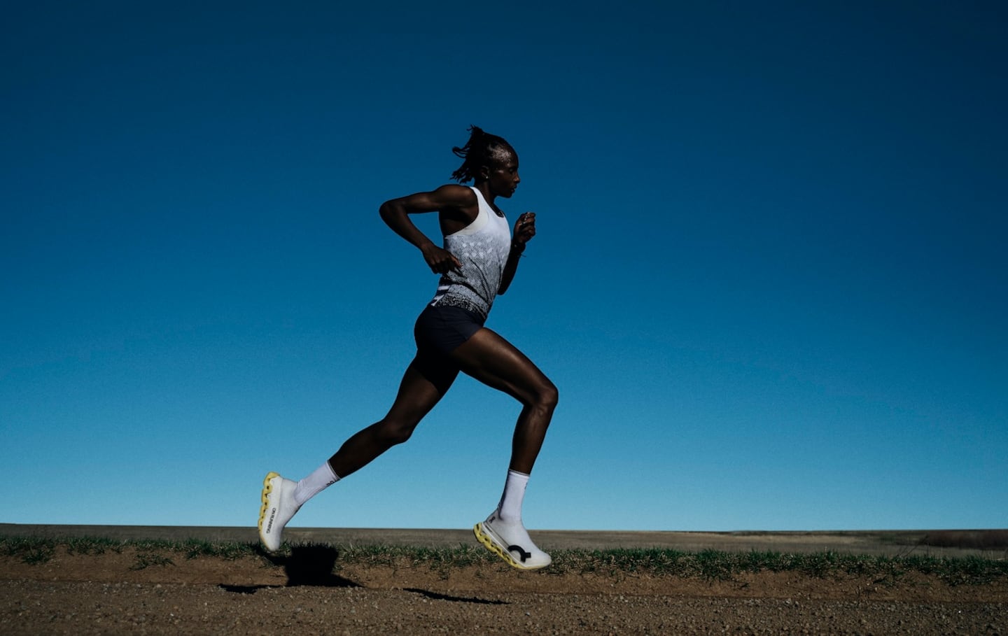 A runner running in On's new white lightspray sneaker model with a blue dusk sky in the backdrop.