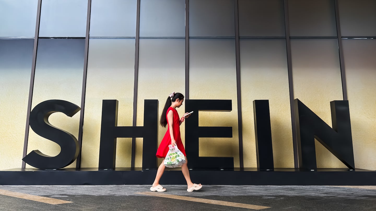 A woman looks at her phone while walking past a Shein sign outside the company's office in Guangzhou, Guangdong Province, China.
