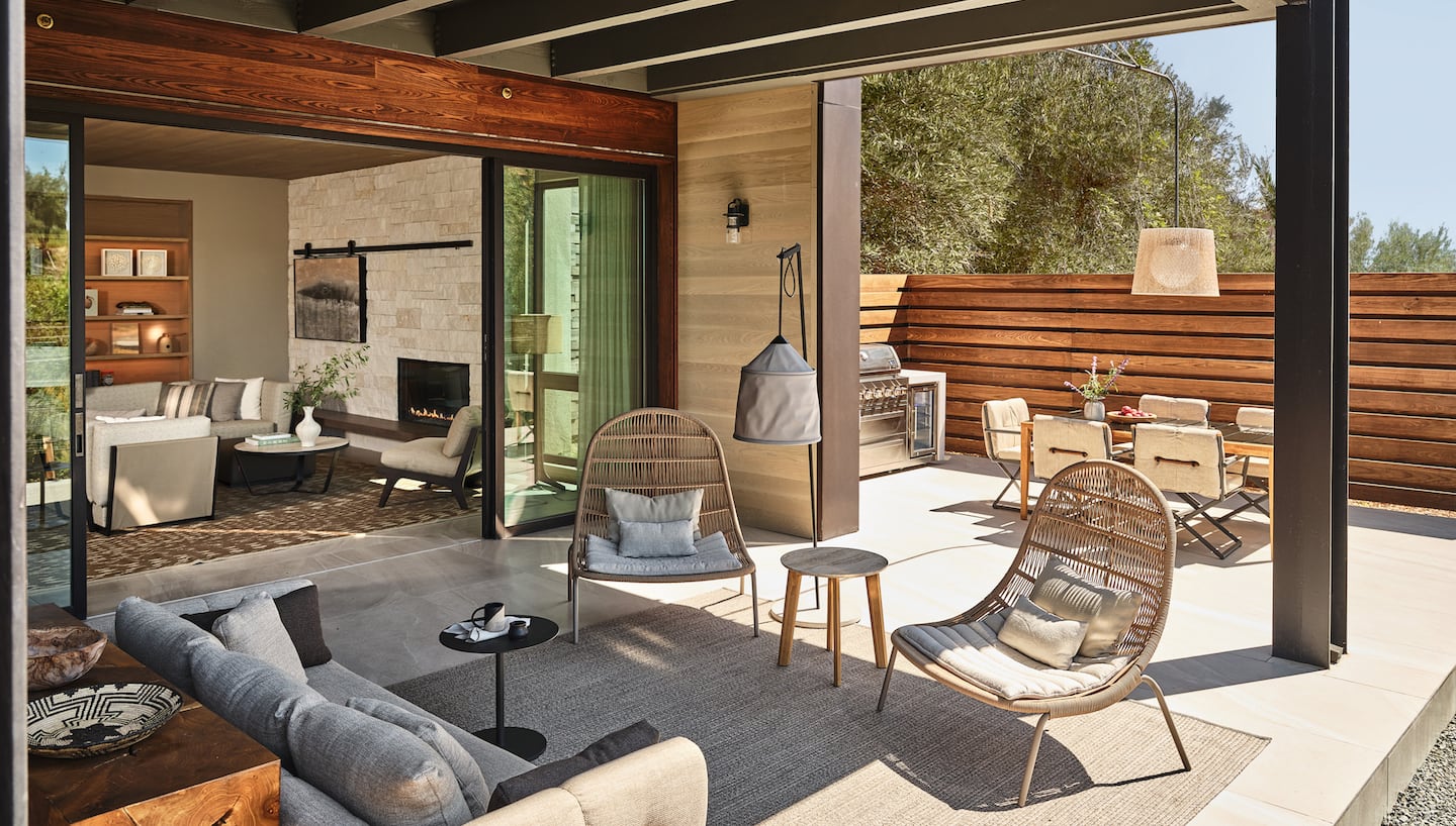 Two chairs face a sofa in an open air seated area, leading to an al fresco dining area on the right and an indoor seated area on the left.