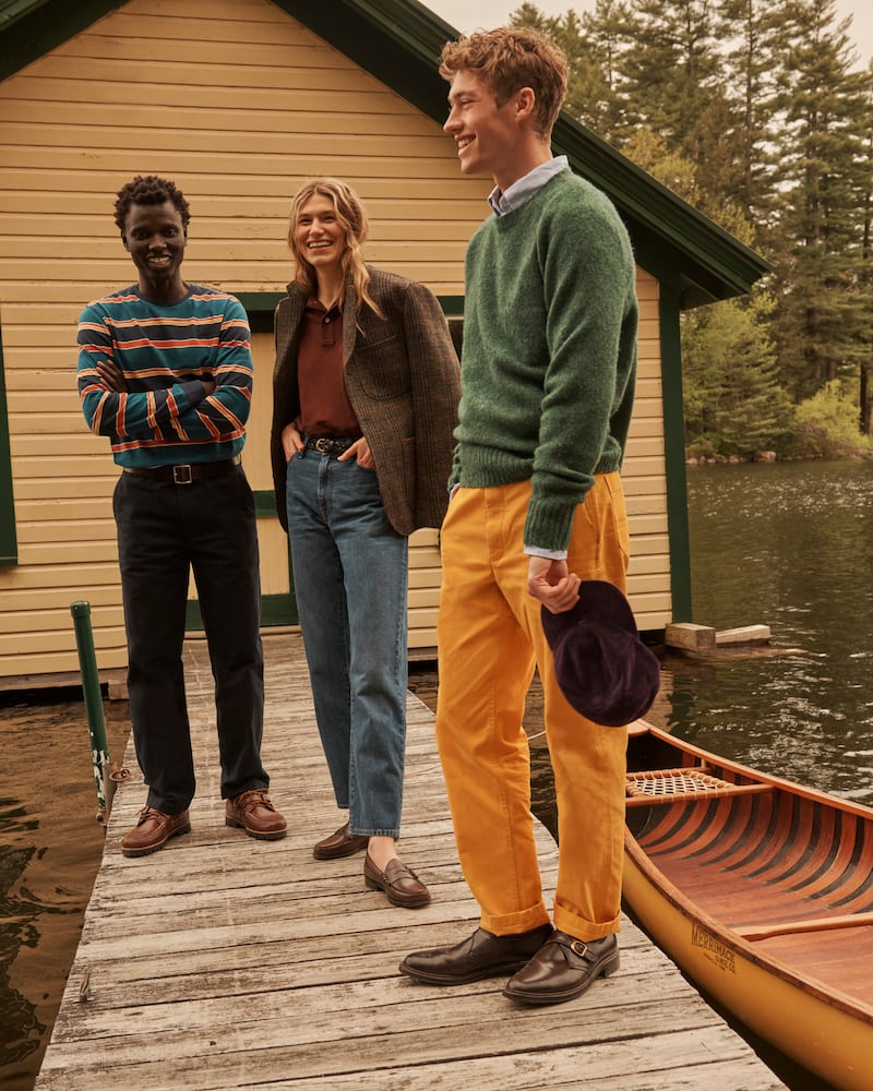 Two men and a woman, three models dressed in prep, stand next to a canoe.
