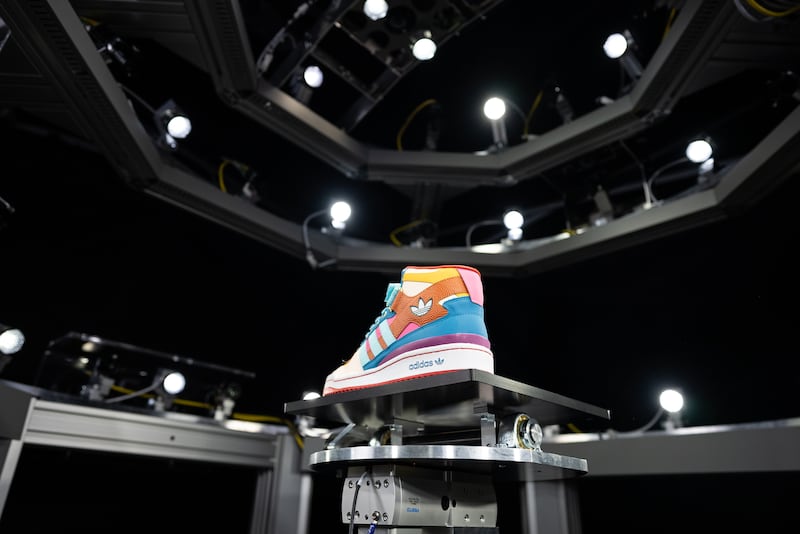 An Adidas sneaker sits in the center of a structure mounted with lights and cameras.