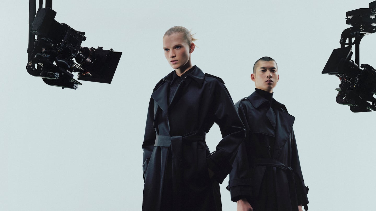 Two models in black trench coats stand against a white backdrop. The coats are made using a new fibre designed to replace polyester and other oil-based materials.