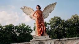 An AI-generated image shows a model in a copper dress standing in front of a winged statue.