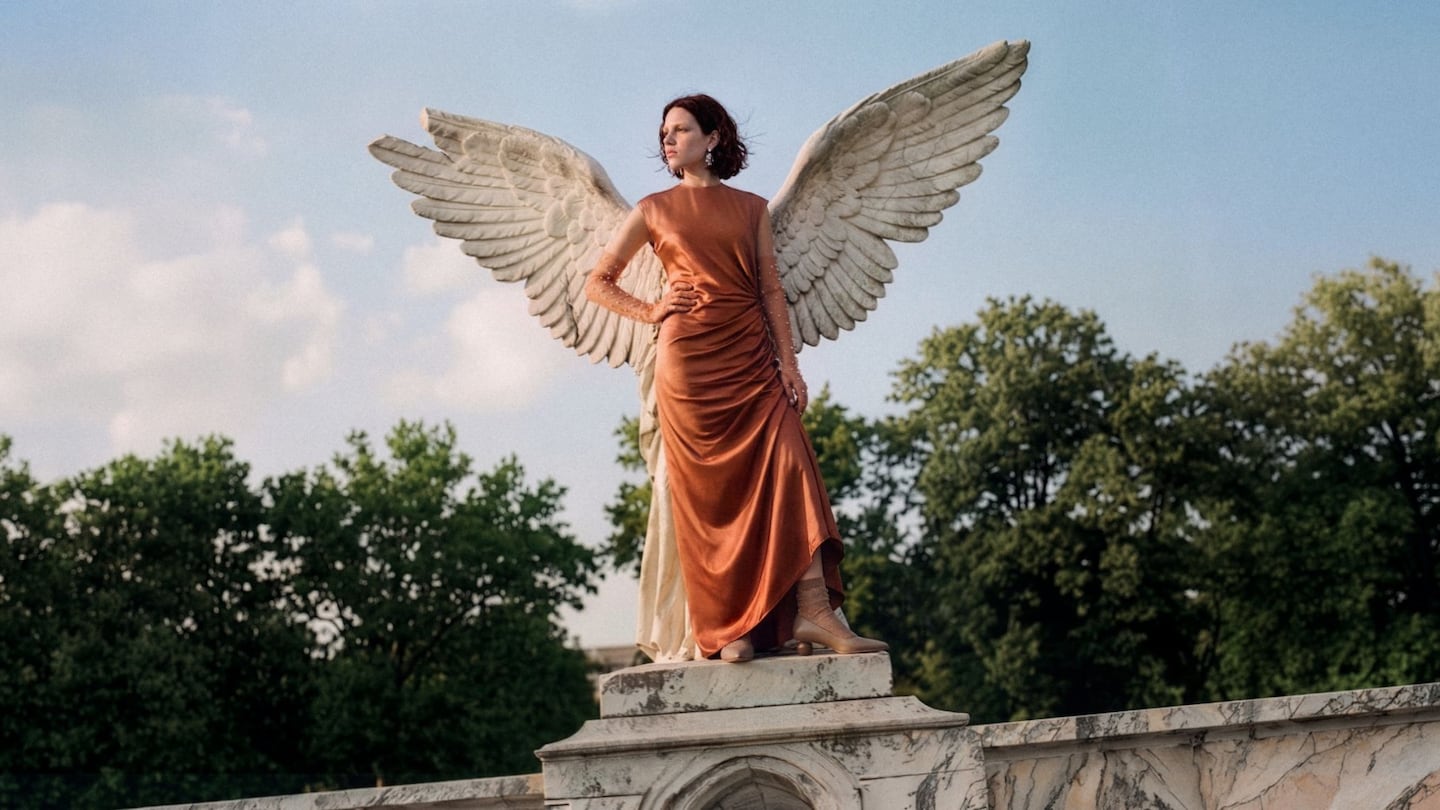 An AI-generated image shows a model in a copper dress standing in front of a winged statue.