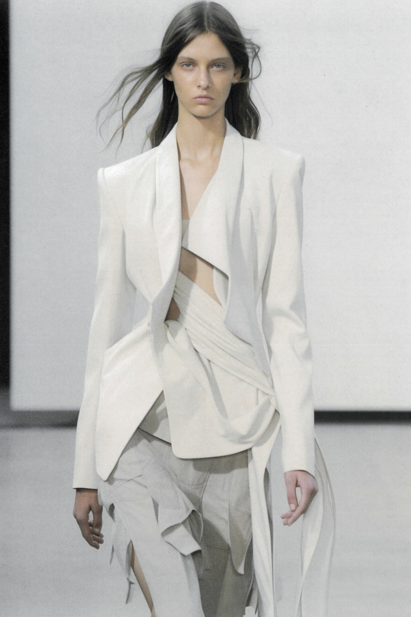 A model in an asymmetrical white blazer walks the runway at Heliot Emil Spring-Summer 2024.