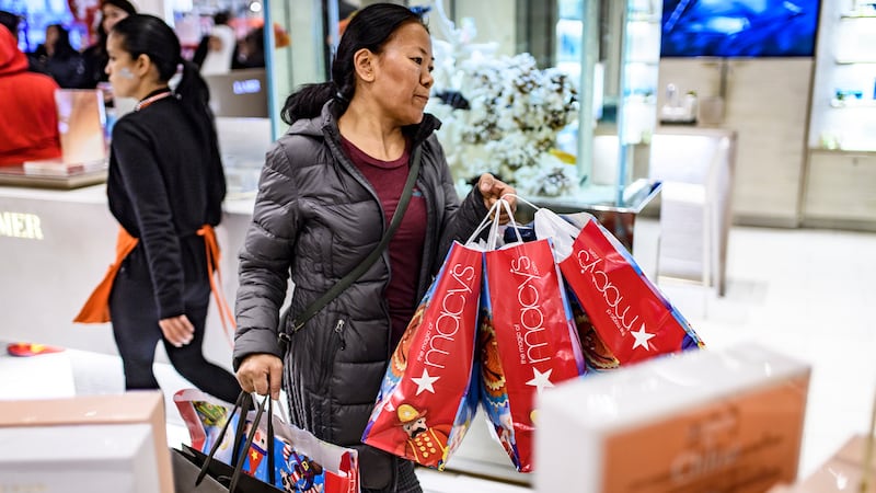 Shopper in Macy's with three bags of shopping in red paper bags.