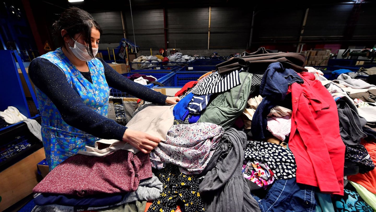 A woman in a blue works in front of a pile of clothes at recycling centre in France.