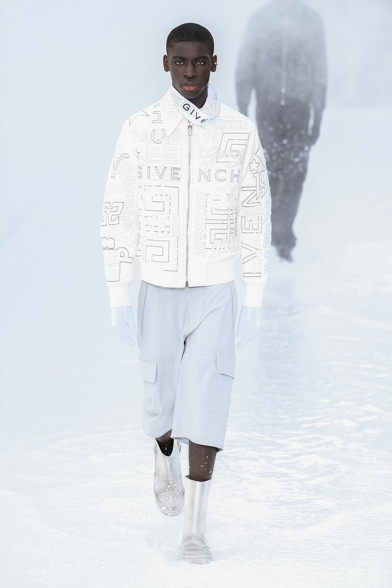 A model wears a white Givenchy embossed bomber jacket with relaxed fit and cropped cargo trousers.