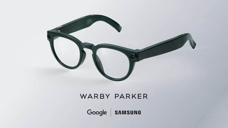 A pair of smart glasses with slightly thicker arms than normal glasses and two very small cameras at the temples sits on a grey background.