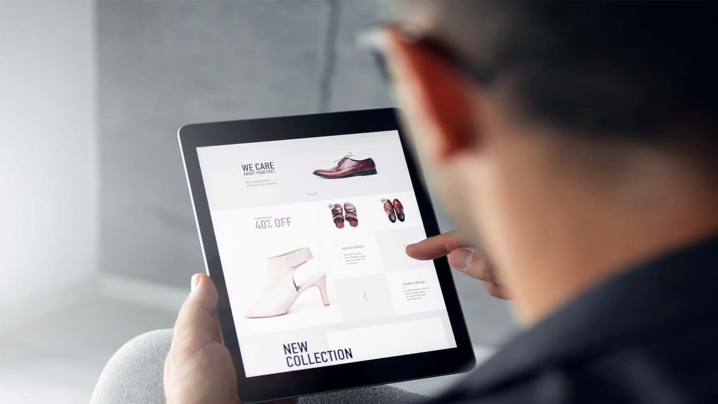 A man holds his finger over a tablet with a fashion e-commerce site open.