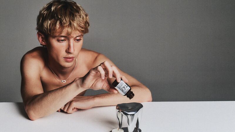 Troye Sivan adds drops to an oil burner resting on a table