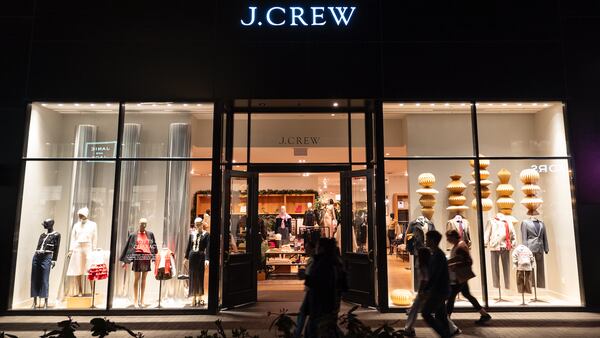 The exterior of a J.Crew store at night with the window display lit up as customers walk past.