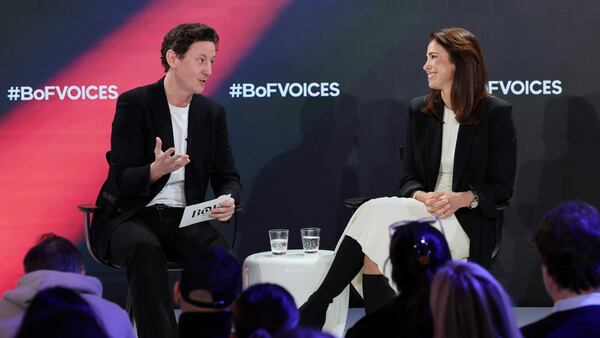 Two figures sit onstage in conversation, the left figure gestures while the right figure sits, smiling. Behind them, a screen reads "#BoFVOICES".