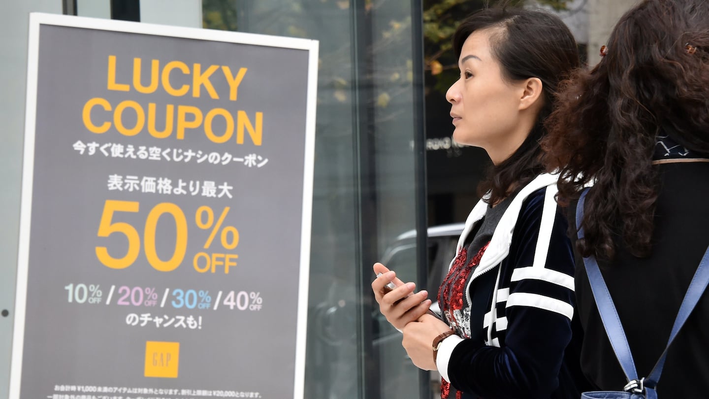 A Japanese shopper stands beside a sign advertising a sale.