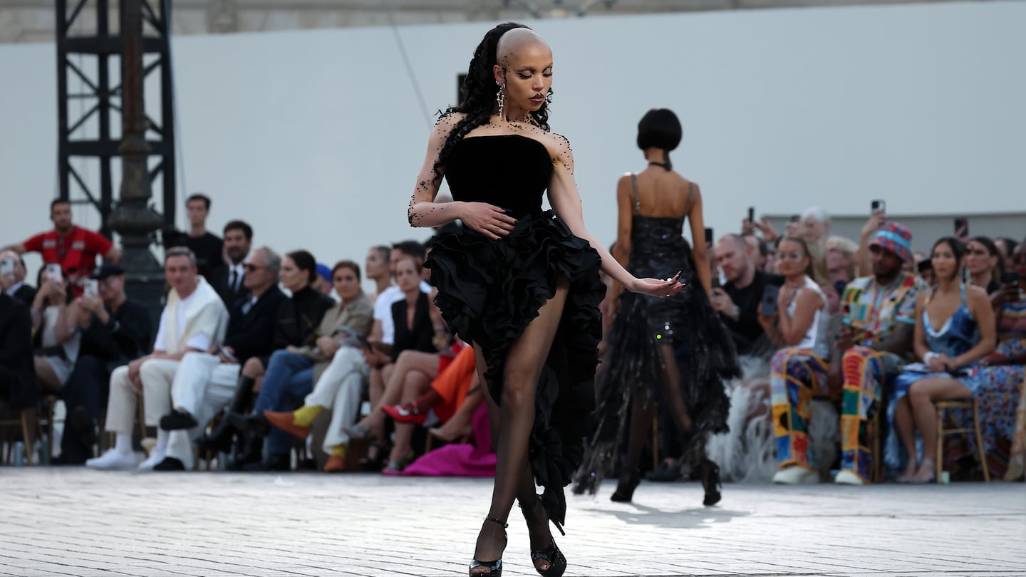 A model walks down a runway wearing a black dress