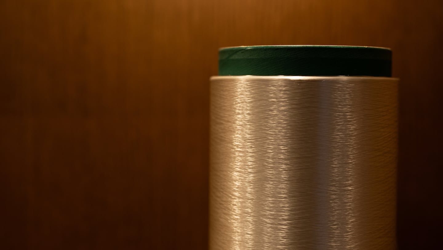 A spool of polyester yarn against a brown background.
