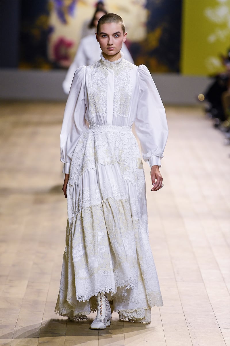 A model wears a white embroidered dress with long sleeves and a white belt.