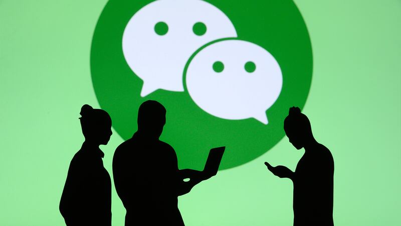 People standing in front of the green WeChat speech bubble logo.