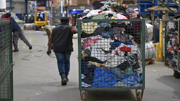 An employee pulls a cage like cart full of second hand clothes receiving for sorting at a recycling facility.
