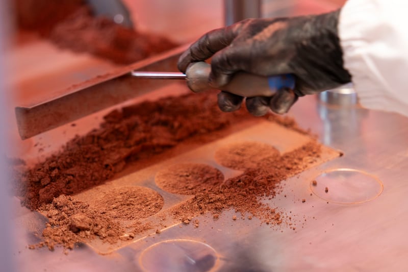 A gloved hand works powdered bronzers into an industrial mould, close up at a beauty product manufacturing facility