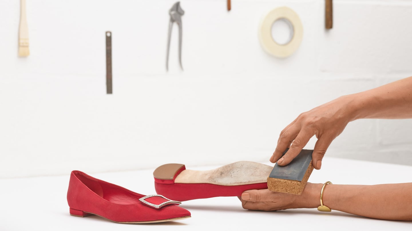 A pair of hands sanding down the soles of red Manolo Blahnik flats.