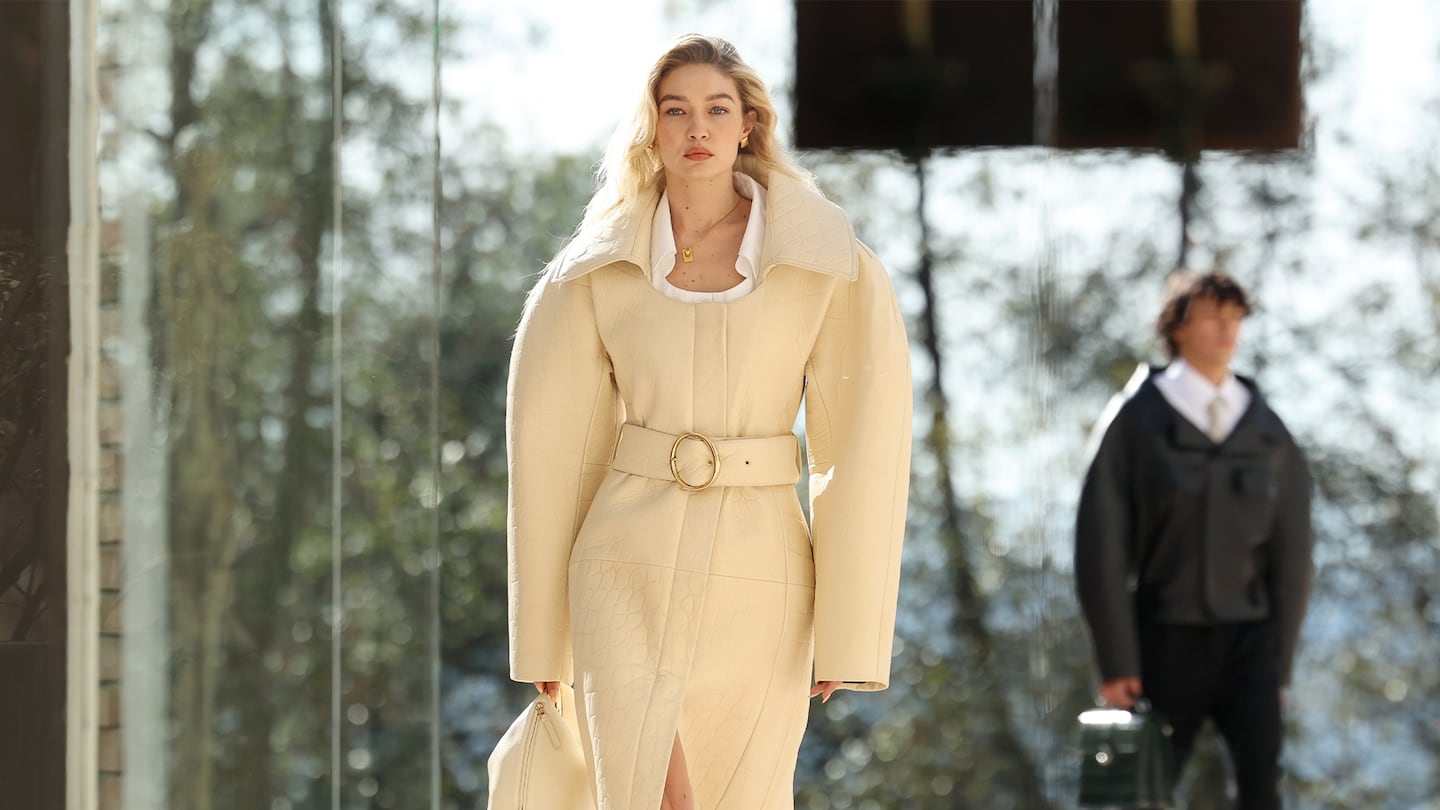 A model walking down the runway. She is wearing a beige coat.