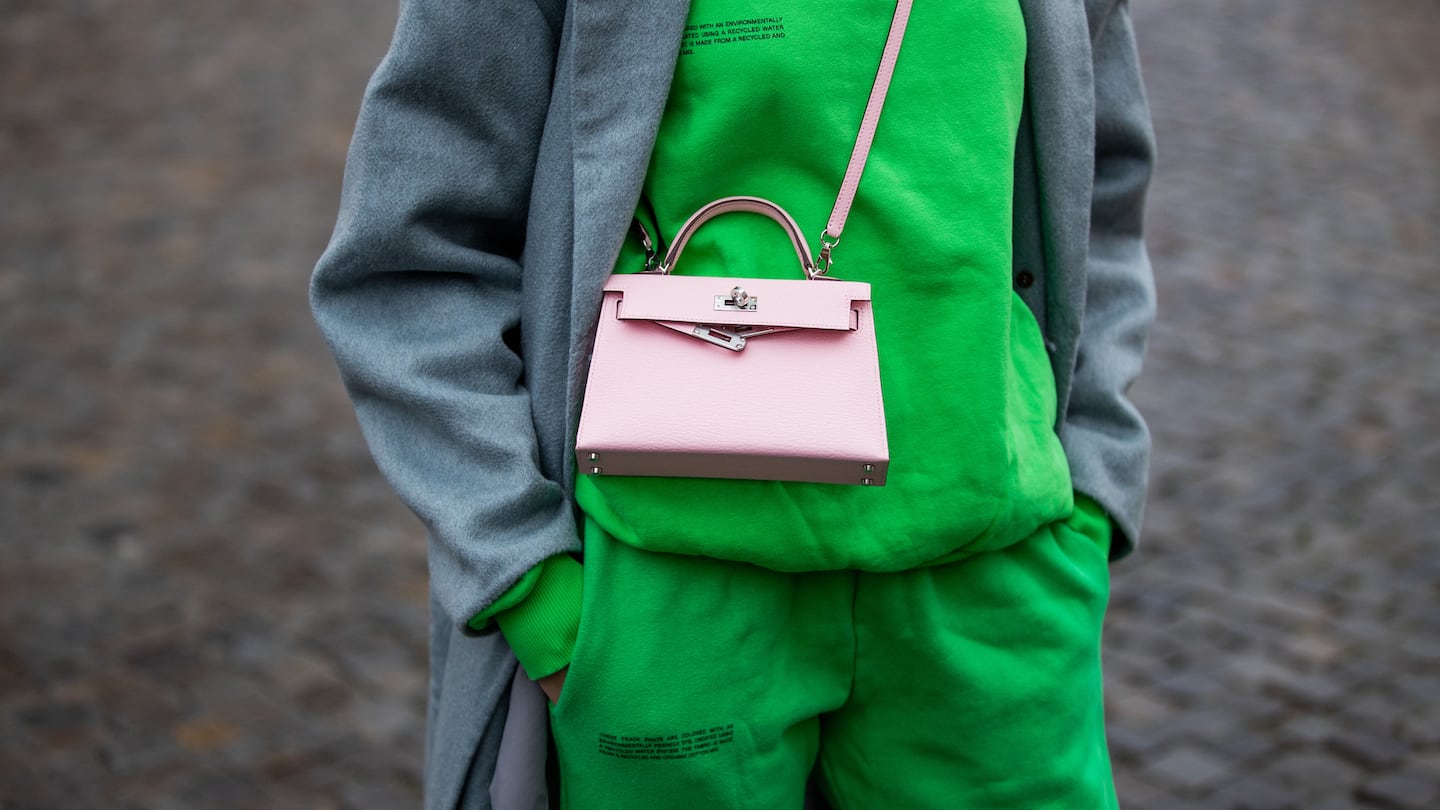 A woman wears a bright green Pangaia sweat suit paired with a grey coat and pink cross-body bag.