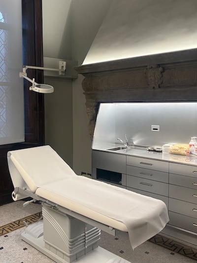 A treatment room at Studio Borbon in Milan, showing a sleek surgical bed and aluminium sink and medical shelf set inside an enormous stone fireplace.