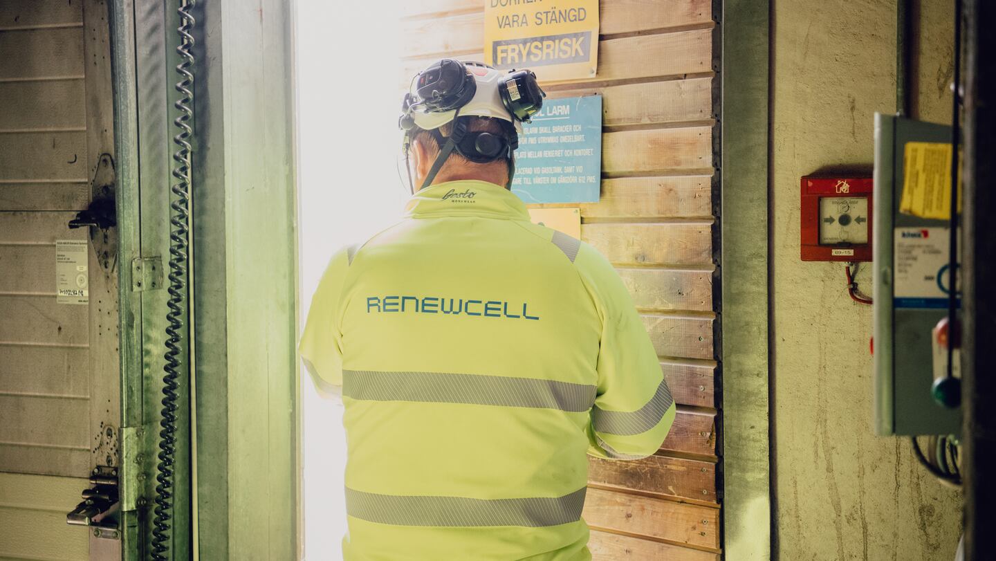 A site manager enters a room in a bright yellow safety jacket with "Renewcell" written on the back.