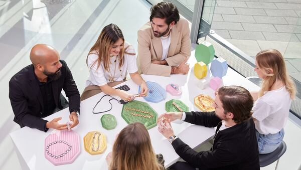 A creative team at work in the Swarovski headquarters. Six figures sit around a table which has crystal-embellished jewellery on display.