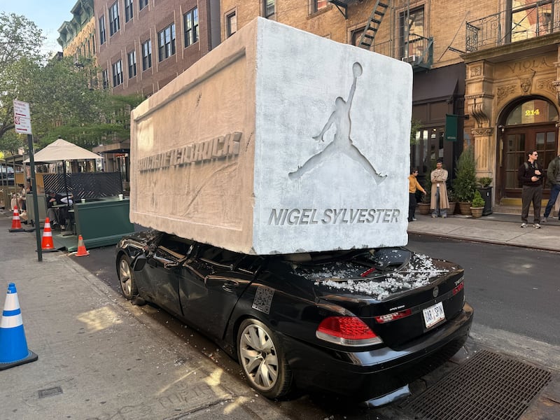 A giant cinderblock with the Air Jordan logo on it on top of a crushed black car on New York City's Mulberry street.