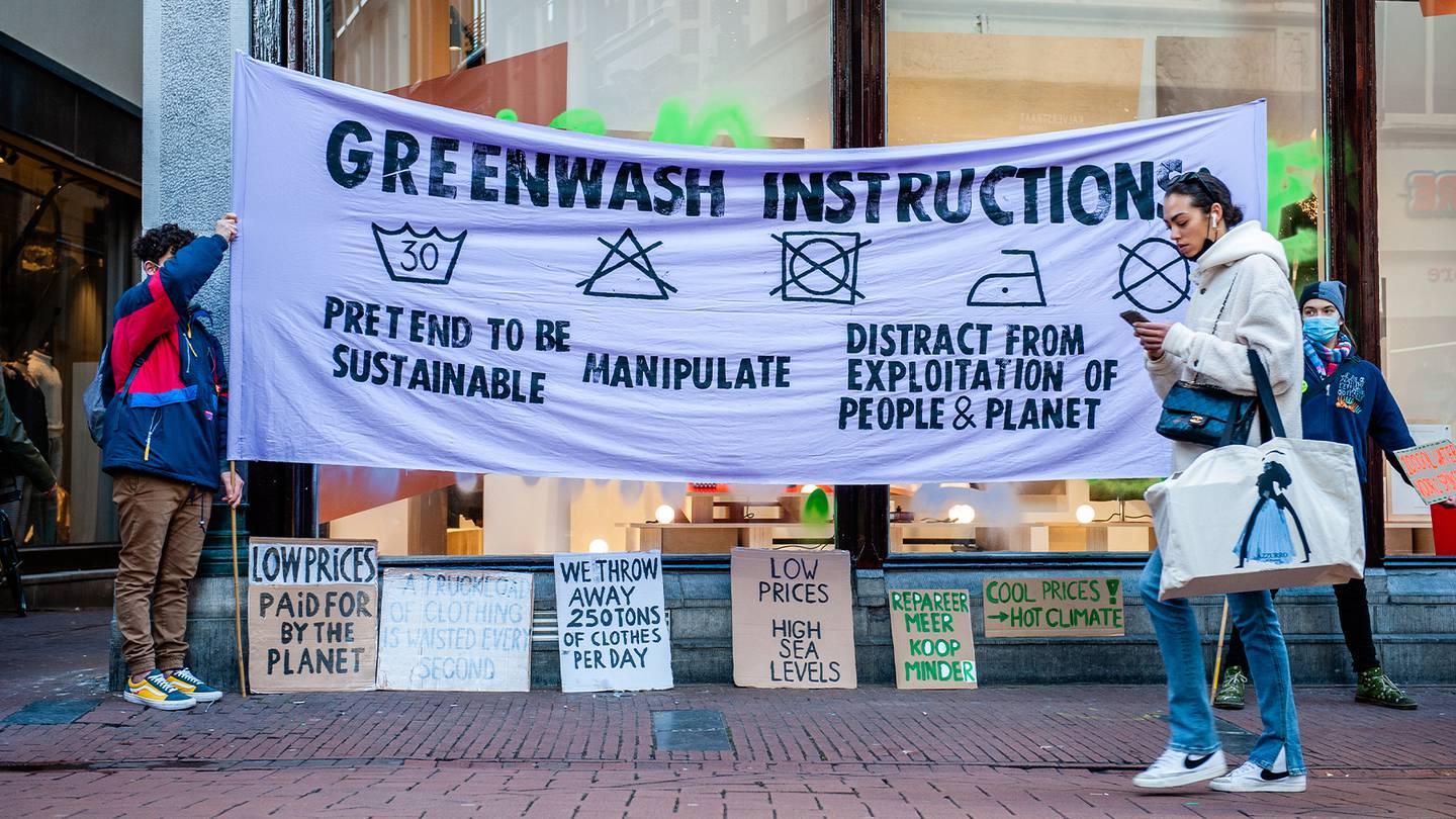 A shopper walks past protesters holding a sign designed to look like a clothing care label with the tag "Greenwashing Instructions."