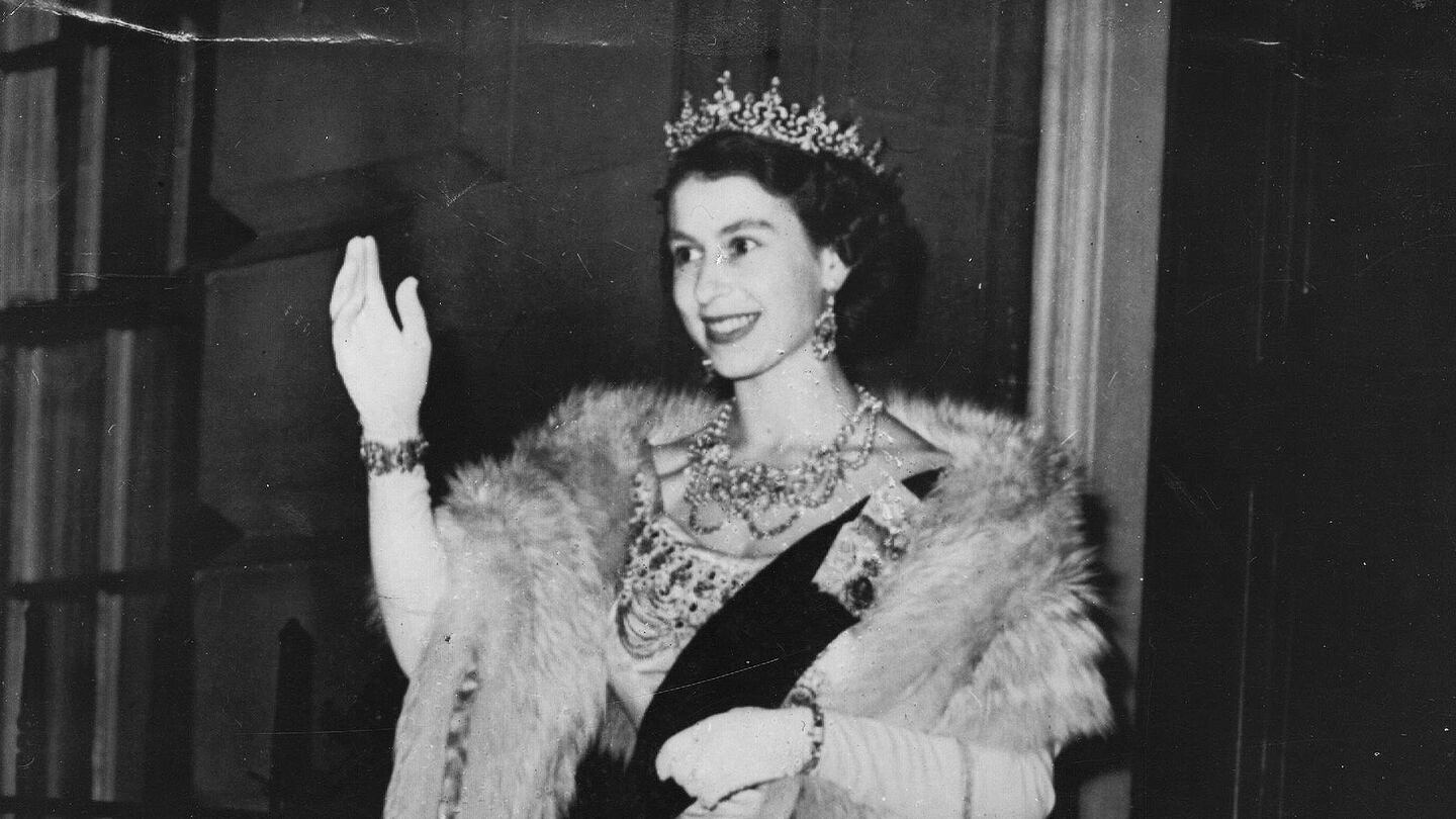 The late Queen Elizabeth II waving to a crowd at a state event.