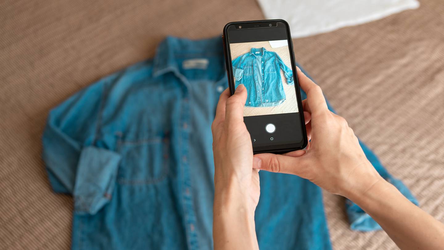 A phone held above a denim shirt takes a picture of the garment.
